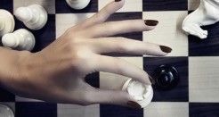 mano con las uñas pintadas de negro encima de un tablero de ajedrez