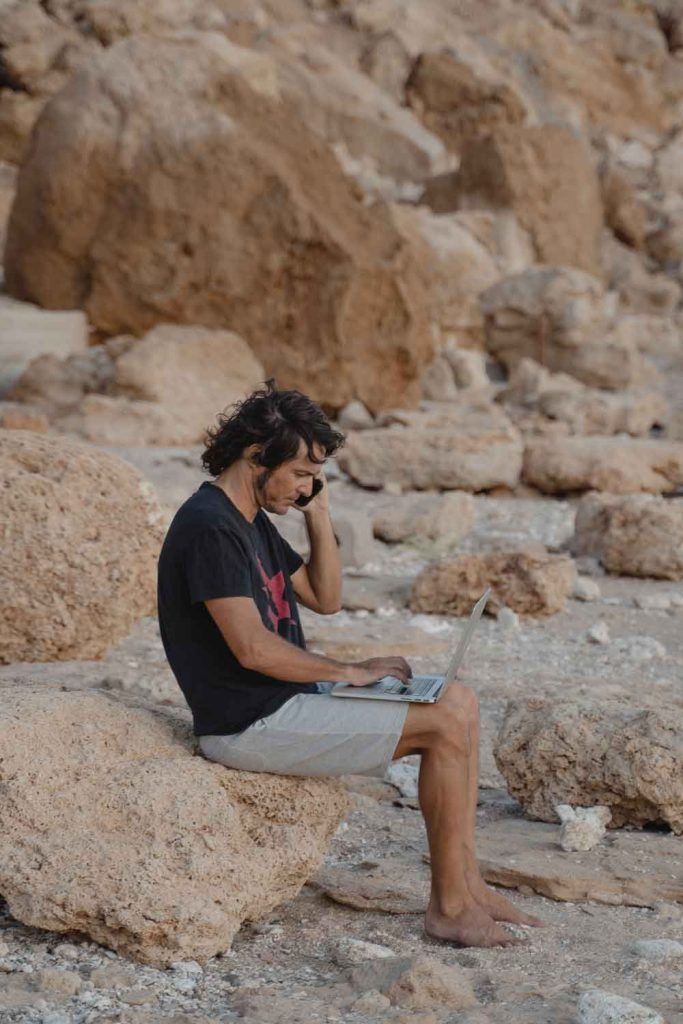 chico trabajando en la playa con movil y ordenador