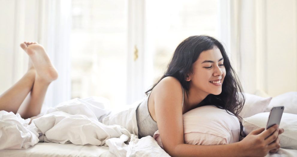 chica joven tumbada sobre la cama mirando el movil.