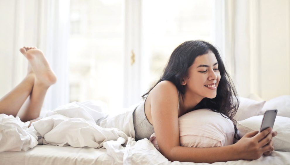 chica joven tumbada sobre la cama mirando el movil.