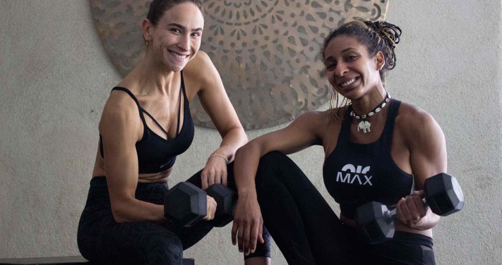 Dos chicas con ropa deportiva y pesas sentadas en actitud relajada y feliz
