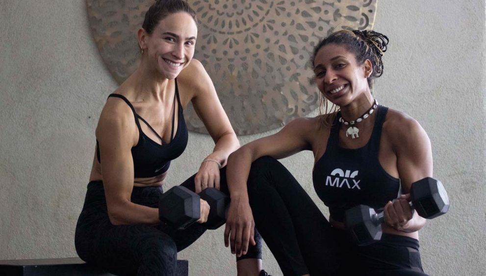 Dos chicas con ropa deportiva y pesas sentadas en actitud relajada y feliz