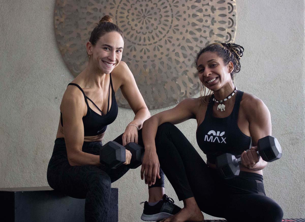 Dos chicas con ropa deportiva y pesas sentadas en actitud relajada y feliz