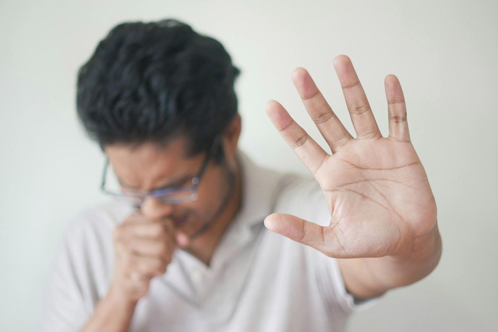 hombre tosiendo mano cubre boca palma de la otra mano en actitud espera