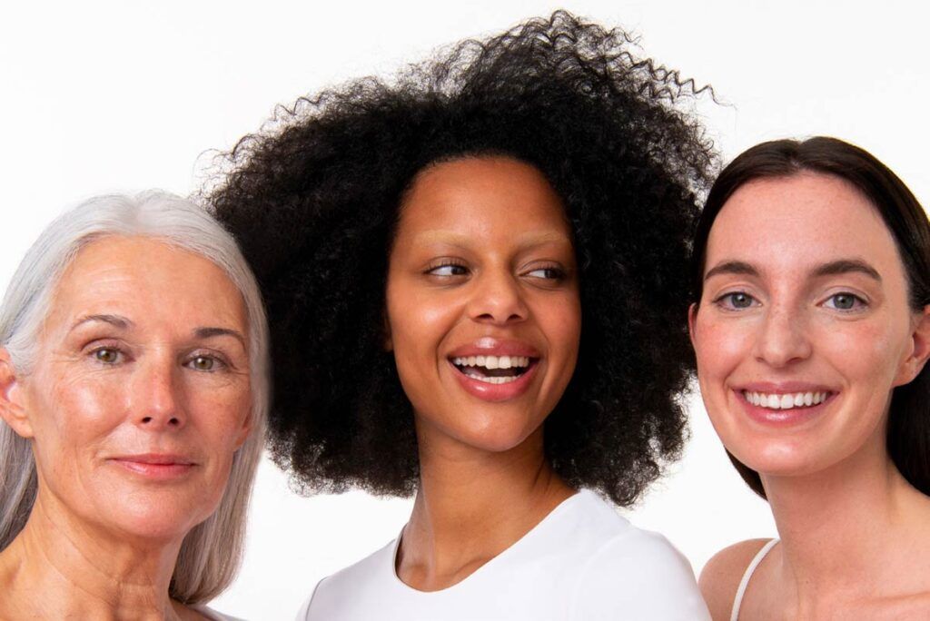 3 mujeres, madura pelo blanco, negra joven pelo rizado y morena pelo liso, sonrientes