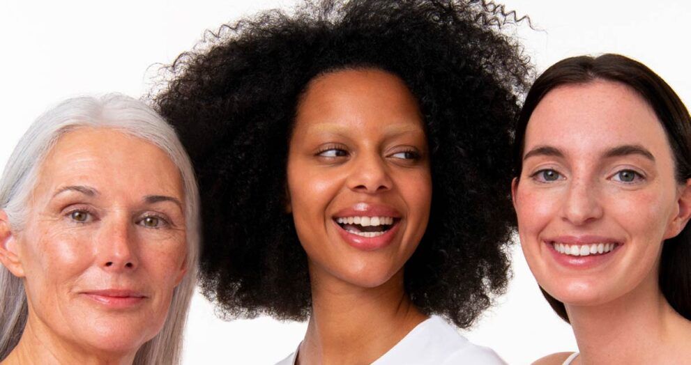 3 mujeres, madura pelo blanco, negra joven pelo rizado y morena pelo liso, sonrientes