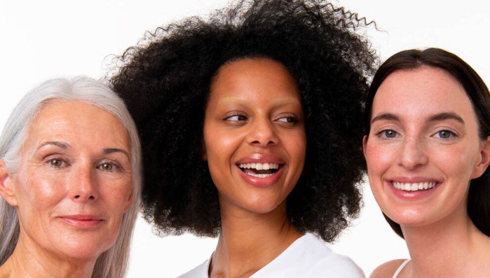 3 mujeres, madura pelo blanco, negra joven pelo rizado y morena pelo liso, sonrientes