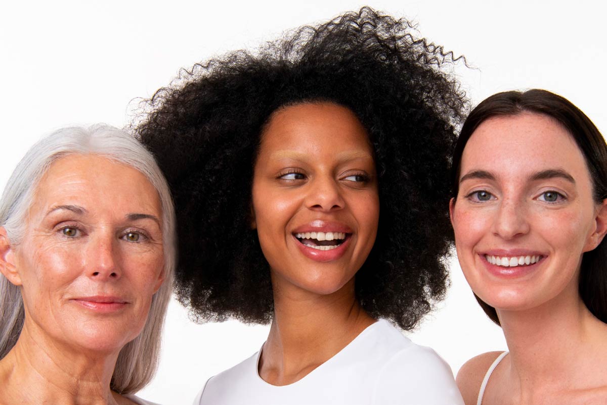 3 mujeres, madura pelo blanco, negra joven pelo rizado y morena pelo liso, sonrientes