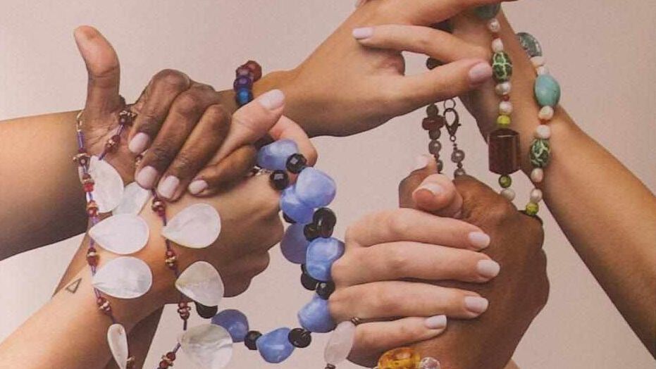 manos de mujeres de distintas razas entrelazadas con cadenas de bisutería reciclada