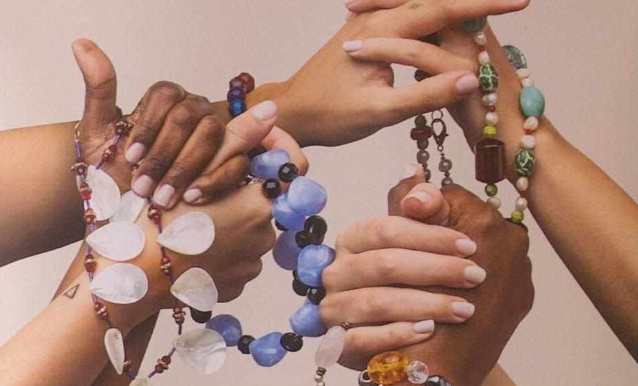 manos de mujeres de distintas razas entrelazadas con cadenas de bisutería reciclada