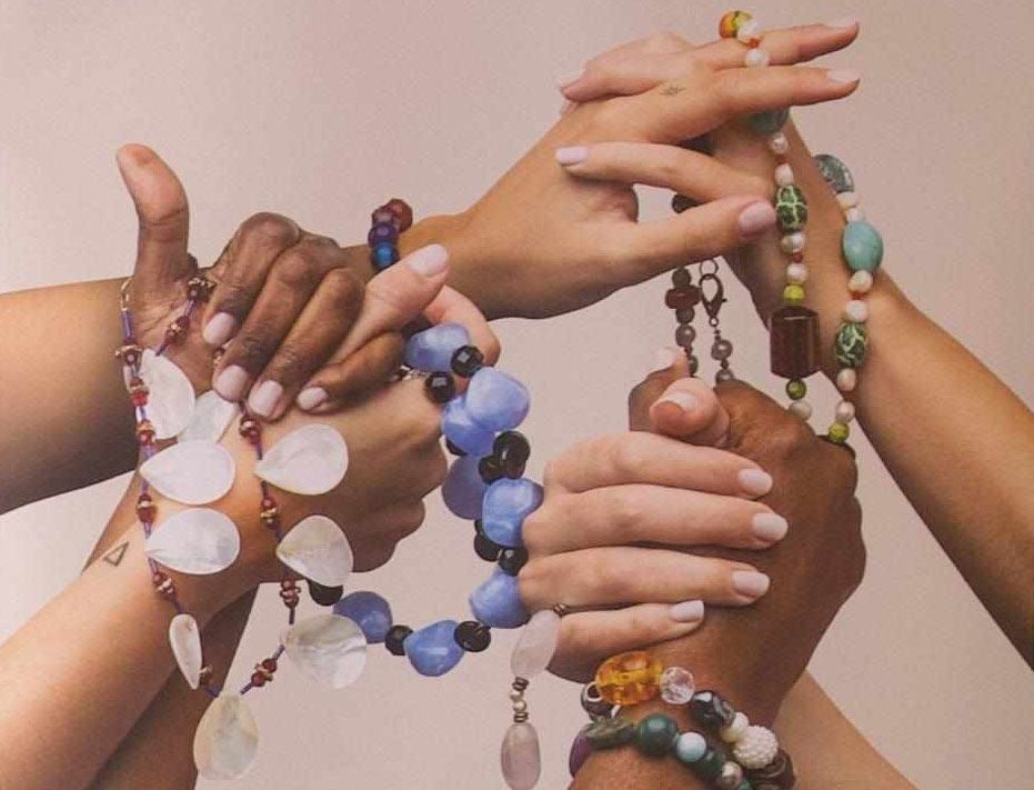 manos de mujeres de distintas razas entrelazadas con cadenas de bisutería reciclada