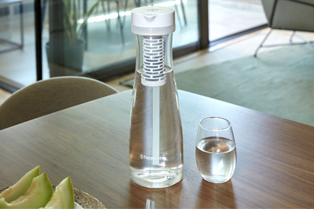 botella con filtro de agua sobre mesa y junto a vaso de agua y rodajas de melón en plato