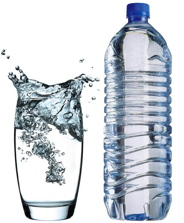 Un vaso de agua filtrada junto a una botella de agua mineral